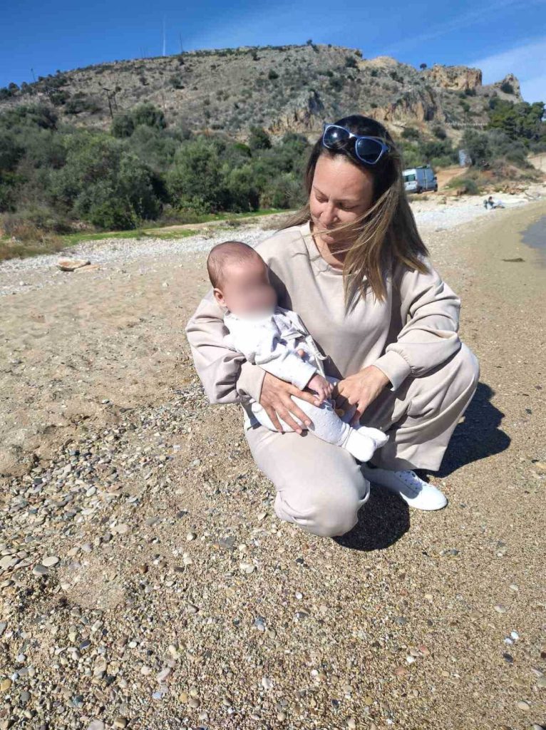 Η Αντωνία Σταματούδη κρατάει το μωρό της στην αγκαλιά της στην παραλία.