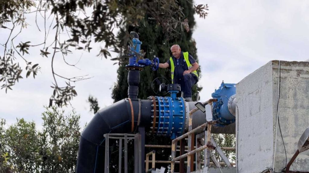 Εργάτης με γιλέκο ασφαλείας ελέγχει βαλβίδα σε μεγάλο αγωγό στον Βιολογικό καθαρισμό