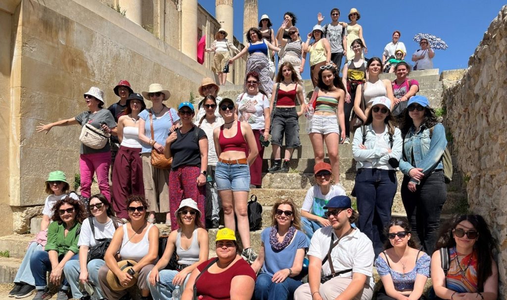 Μεγάλη ομάδα ανθρώπων ποζάρει σε αρχαία πέτρινα σκαλιά.