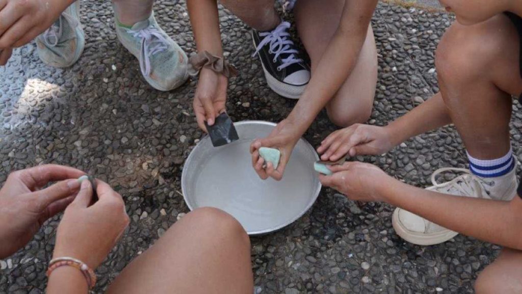 Μια παρέα παιδιών απασχολείται δημιουργικά, λειαίνοντας με προσοχή μικρά κομμάτια πέτρας για τις κατασκευές τους.